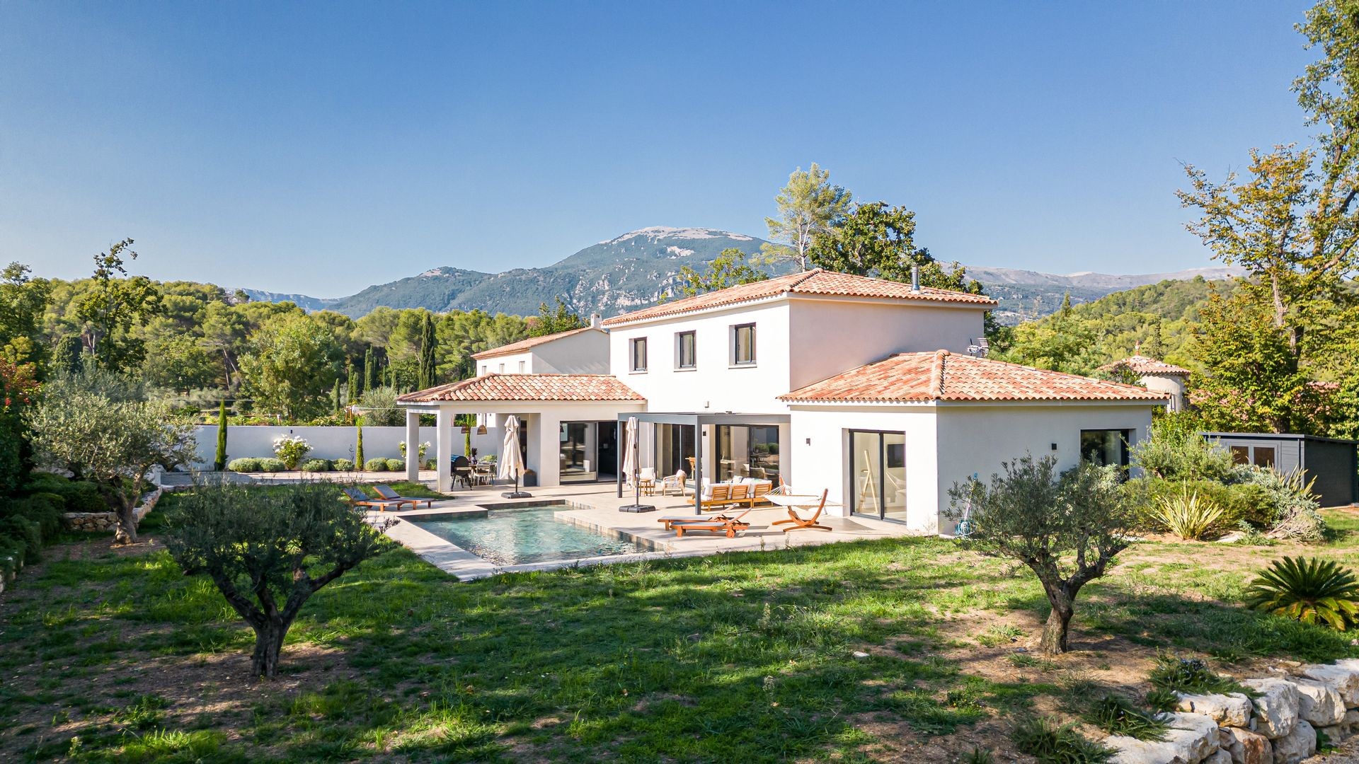 Modern villa with a pool in a lush garden setting, surrounded by trees and mountains.