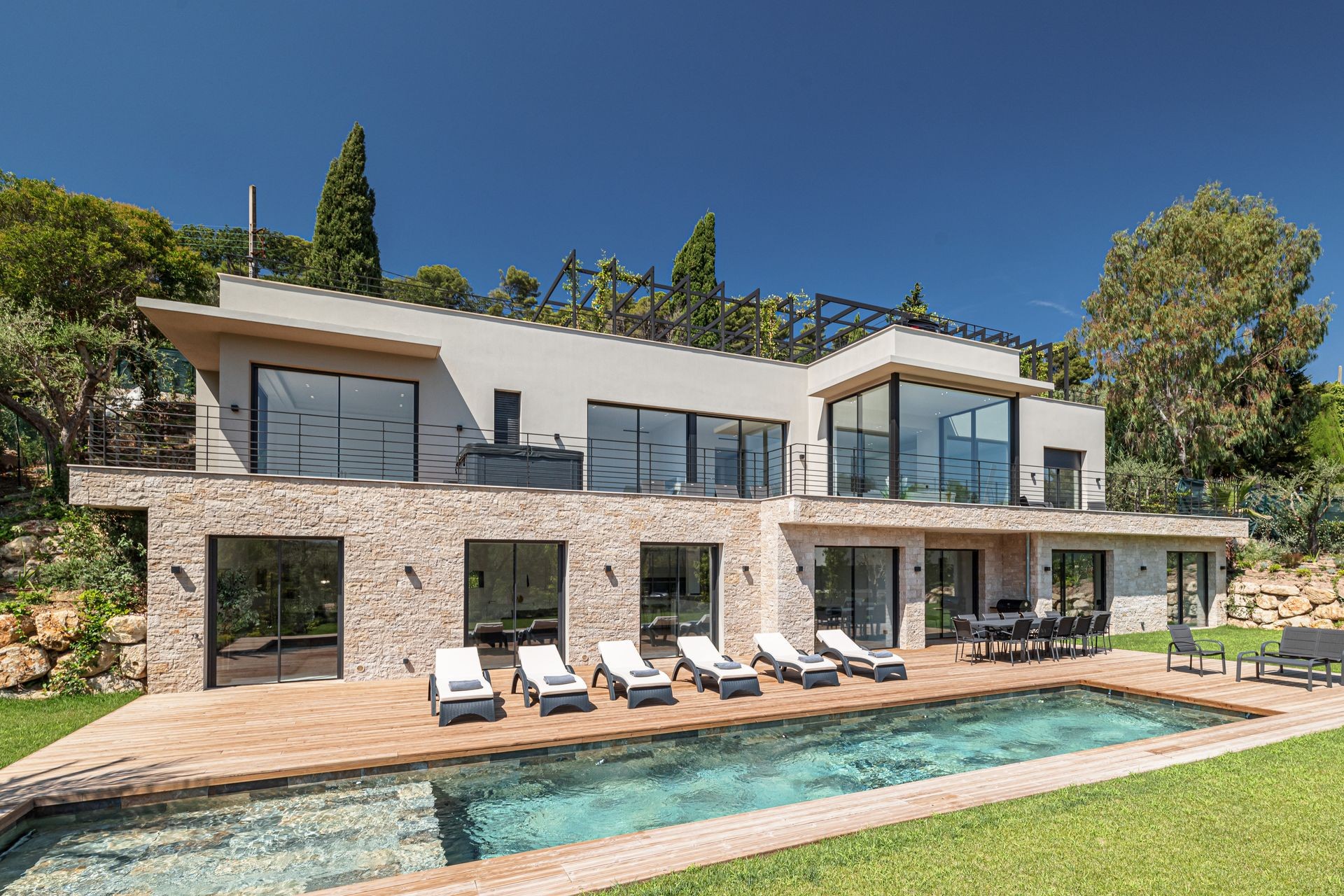 Modern luxury villa with stone facade, deck chairs, and a swimming pool in a landscaped garden.